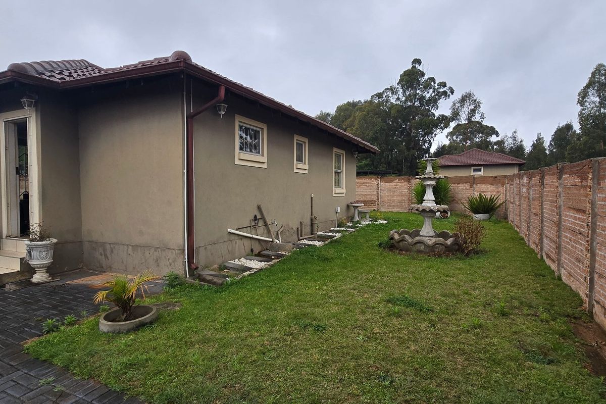 Rear exterior view of the property featuring a paved patio area, a small lawn with a stone fountain, and a brick boundary wall.