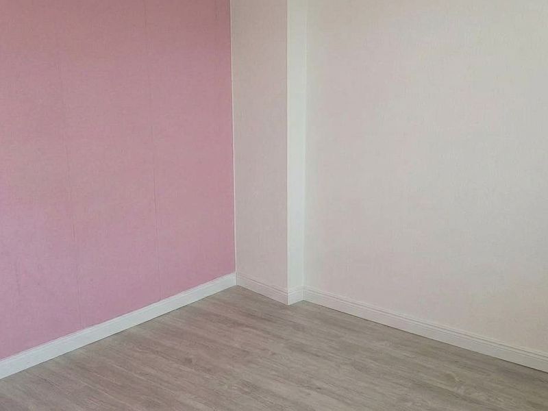 A clean, empty bedroom featuring light-toned laminate flooring and a combination of white and pink painted walls.