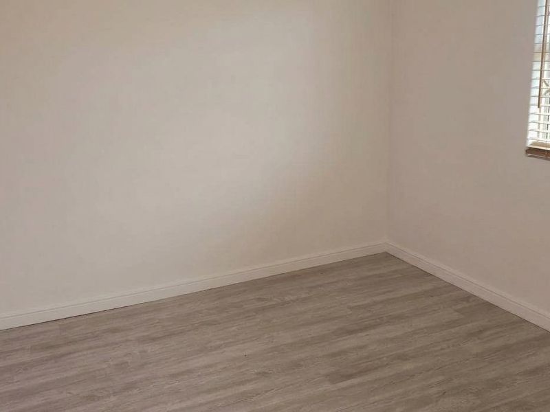 A vacant bedroom featuring light-toned laminate flooring, a window with security bars, and neutral wall finishes.