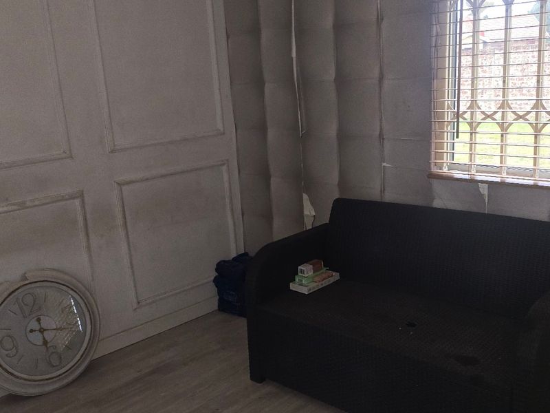 A living room area featuring decorative wall paneling, laminate flooring, and a window fitted with a security gate.