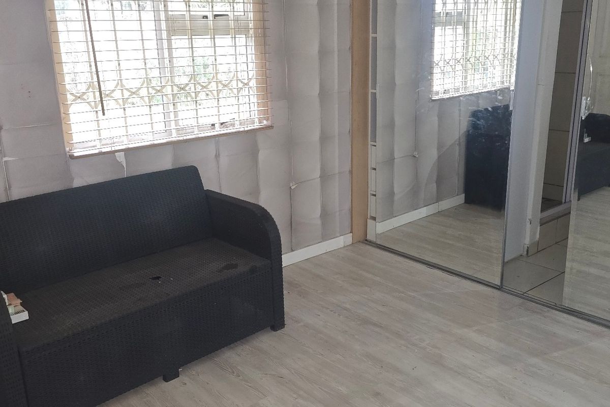 Bedroom featuring built-in cupboards with mirrored sliding doors, laminate flooring, and security bars on the windows.