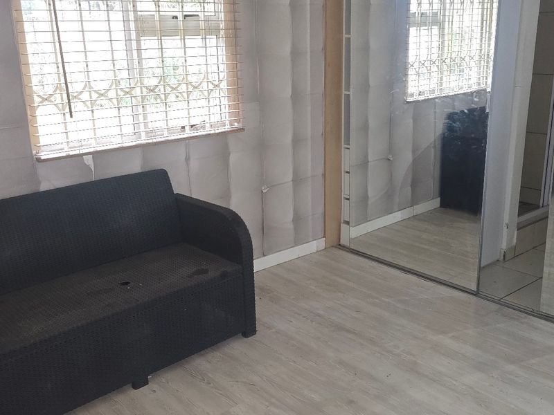 Bedroom featuring built-in cupboards with mirrored sliding doors, laminate flooring, and security bars on the windows.