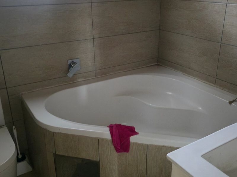 A bathroom featuring a corner bathtub, toilet, and vanity basin with neutral wall tiling.