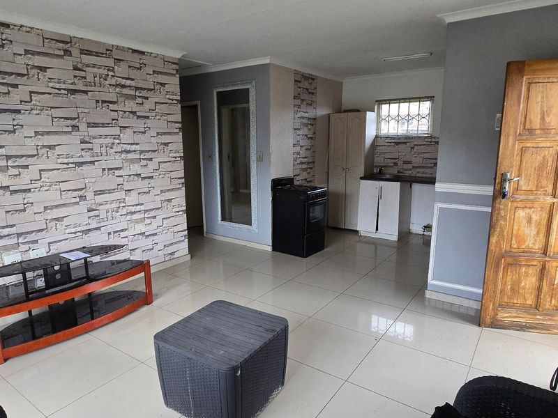 Open plan living area featuring tiled floors, a compact kitchen corner with cabinetry and a freestanding stove, and decorative wall cladding.