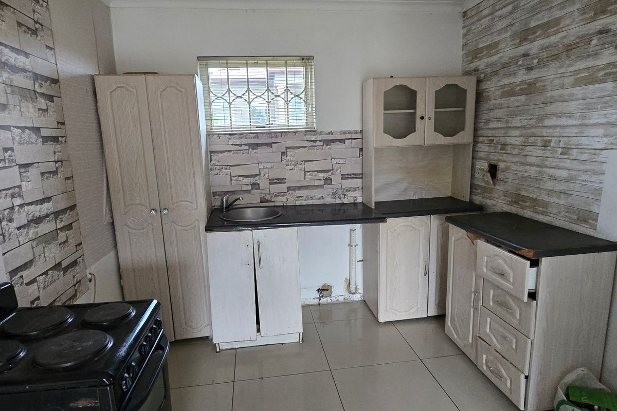 A compact kitchen featuring built-in cabinetry, a stainless steel sink, and an electric stove, requiring cosmetic updates to improve its overall condition.