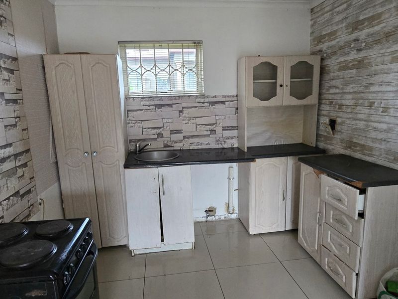 A compact kitchen featuring built-in cabinetry, a stainless steel sink, and an electric stove, requiring cosmetic updates to improve its overall condition.
