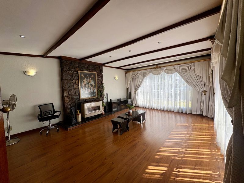 Spacious living room featuring exposed timber ceiling beams, a prominent stone fireplace wall, and warm laminate flooring with ample natural light.