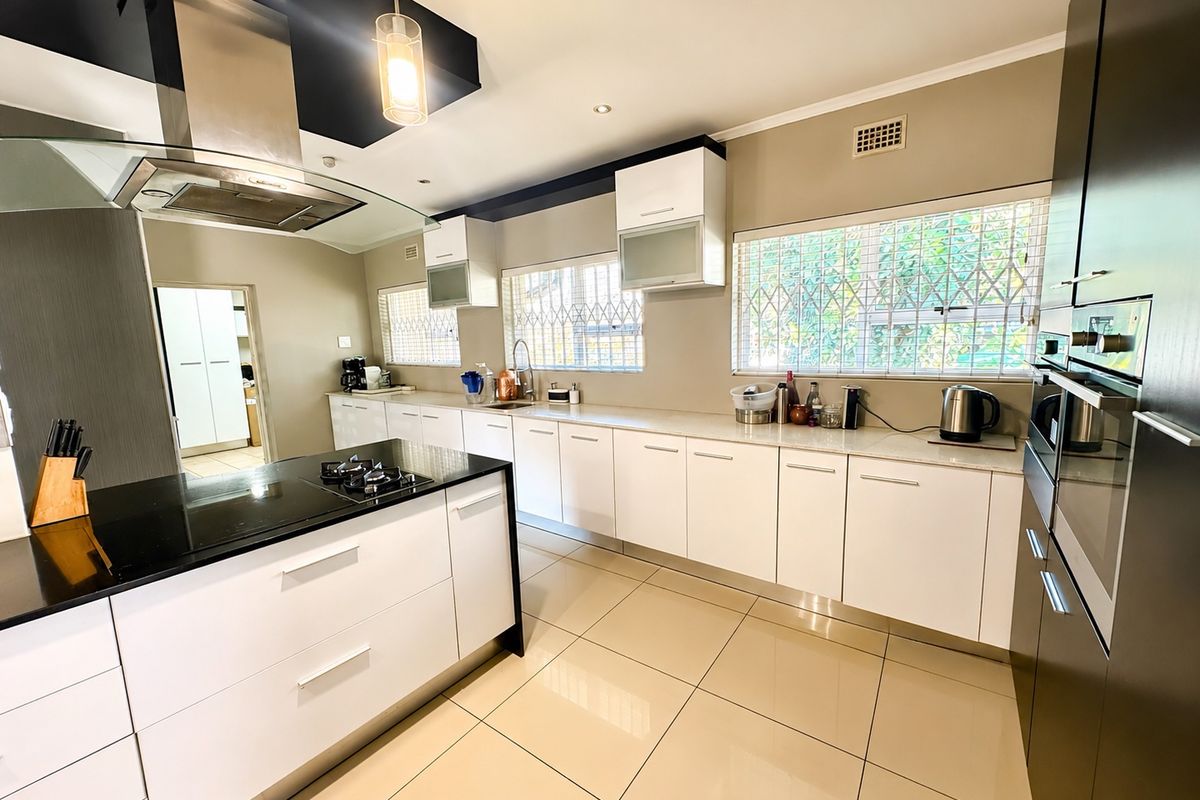 Modern kitchen featuring a central island with gas hob, sleek white cabinetry, integrated oven, and tiled flooring with ample natural light.