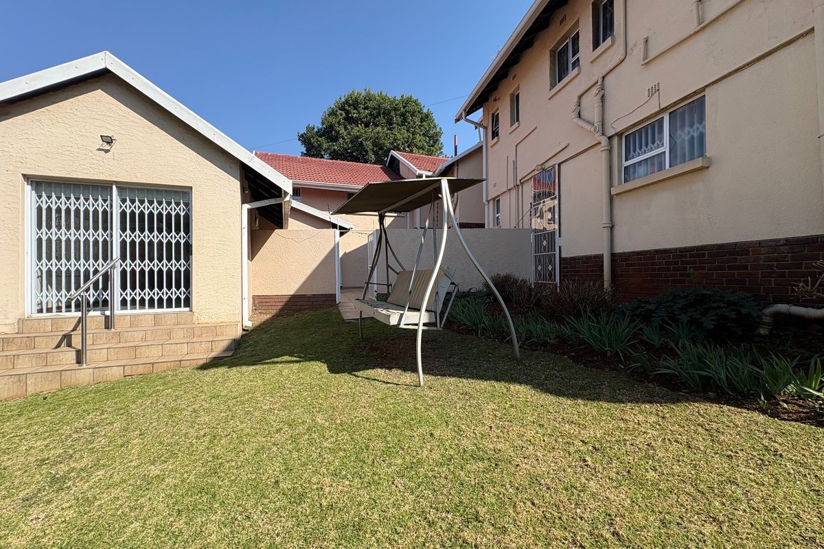 A view of the rear exterior area featuring a small lawn, brick and plastered building facade, and a sliding door with a security gate.