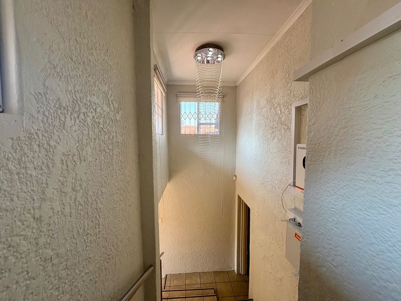A bright, high-ceilinged hallway featuring a staircase, textured wall finishes, and a decorative light fixture.
