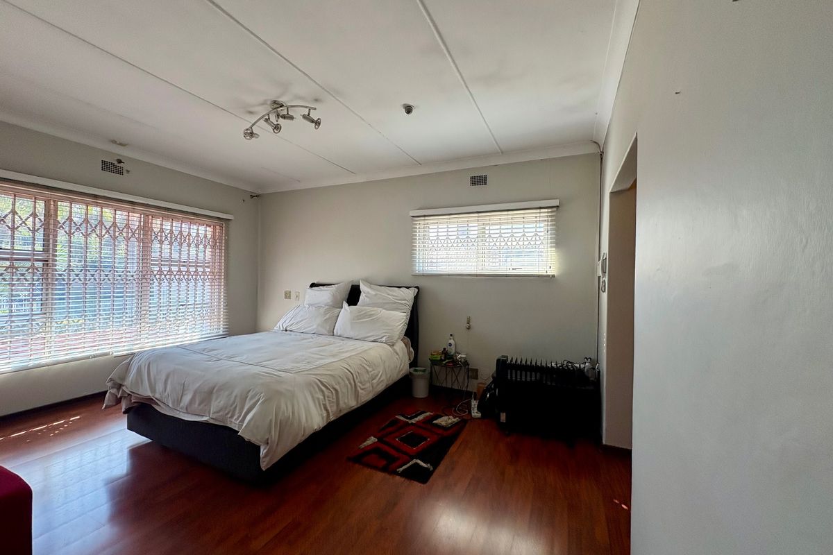 A bedroom featuring laminate flooring, security gates on windows, and venetian blinds, offering a functional space with neutral wall finishes.