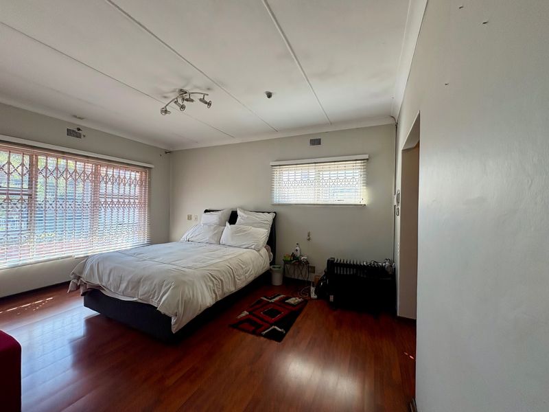 A bedroom featuring laminate flooring, security gates on windows, and venetian blinds, offering a functional space with neutral wall finishes.