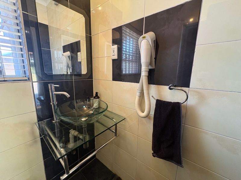 A modern bathroom vanity area featuring a glass vessel sink, chrome mixer tap, wall-mounted hair dryer, and contrasting black and cream wall tiling.