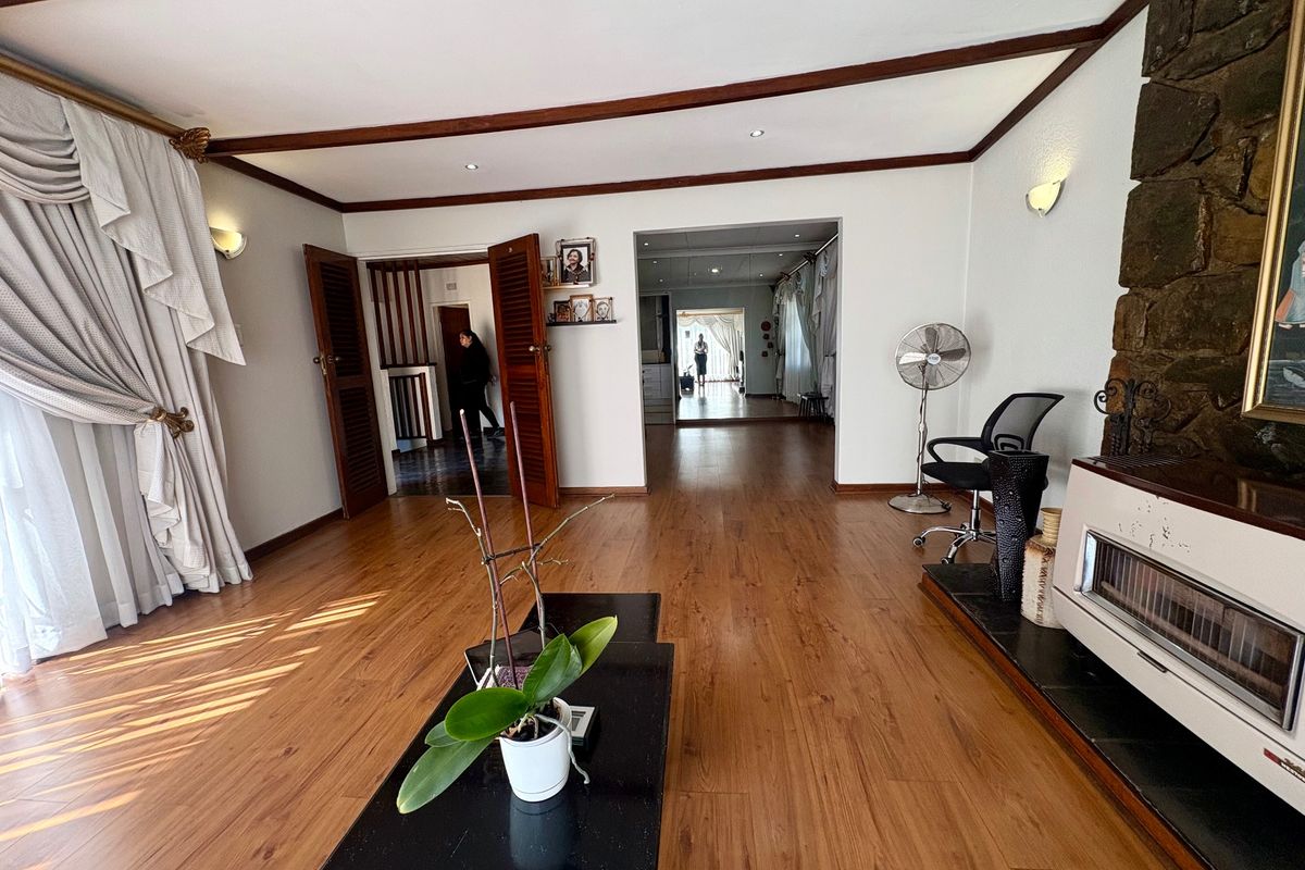 Spacious living room featuring laminate flooring, exposed ceiling beams, and a prominent stone fireplace, offering a warm and inviting atmosphere.