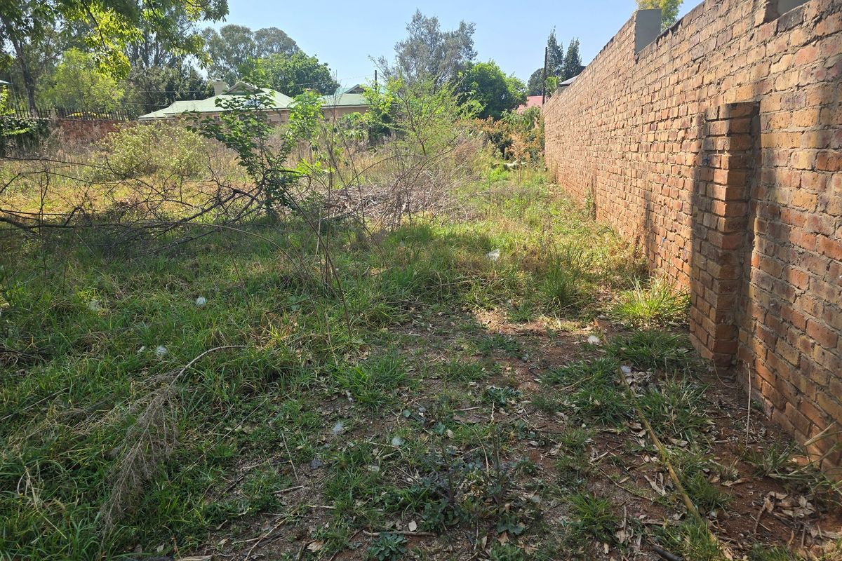 A vacant residential plot featuring an existing brick boundary wall and overgrown natural vegetation.