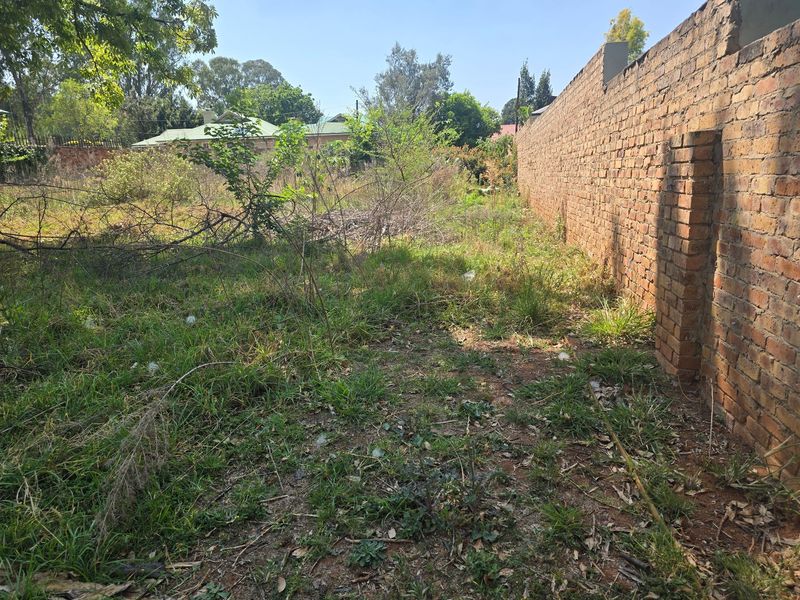 A vacant residential plot featuring an existing brick boundary wall and overgrown natural vegetation.