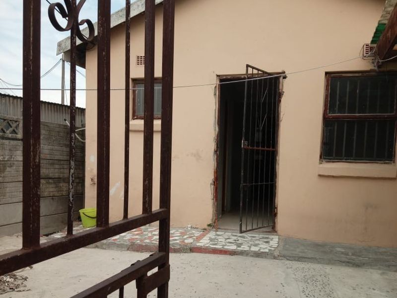 Front view of a residential property featuring a metal security gate, concrete driveway, and security bars on the windows.