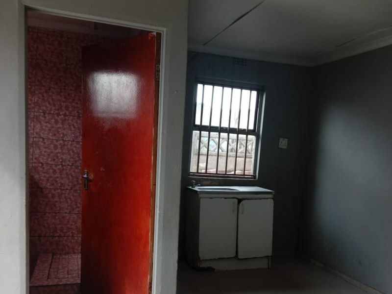 An open-plan living area featuring tiled floors, a small kitchen sink unit, and an adjacent bathroom, presenting a blank canvas for renovation.