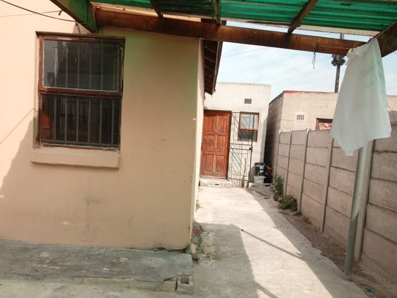 Rear exterior area featuring a concrete patio covered by a timber and corrugated plastic roof, enclosed by a precast concrete boundary wall.