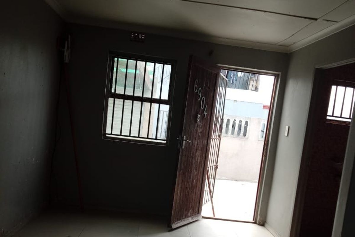 An empty living area featuring tiled flooring, security gate, and burglar bars, offering a functional space ready for renovation or staging.