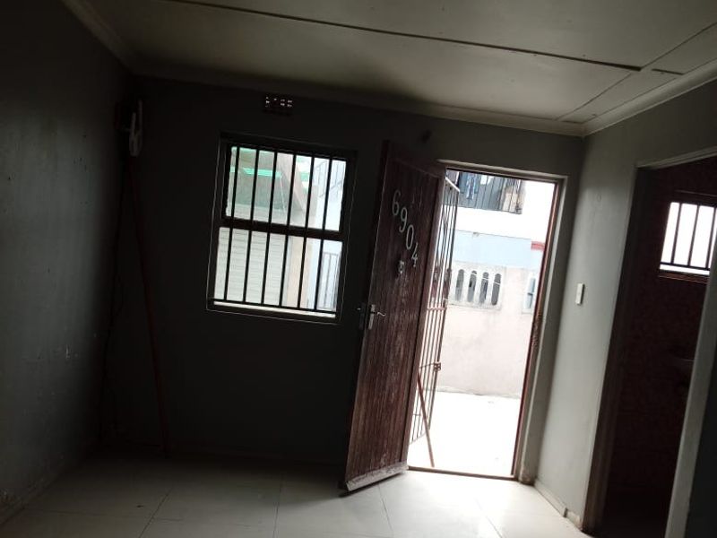 An empty living area featuring tiled flooring, security gate, and burglar bars, offering a functional space ready for renovation or staging.