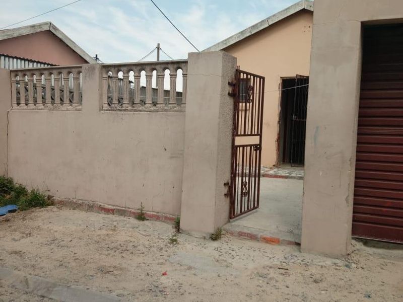 Front exterior view of the property featuring a boundary wall with decorative balustrades, a metal pedestrian gate, and a roller shutter garage door.