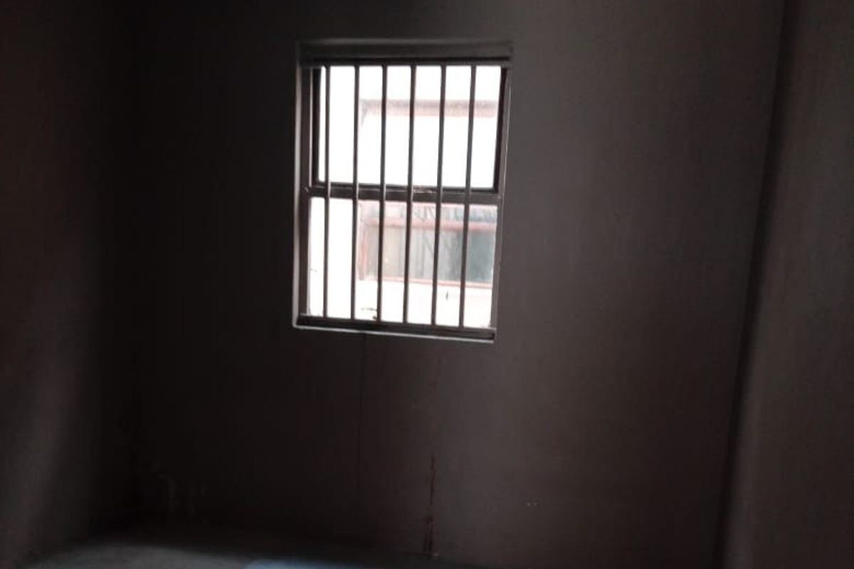 An empty bedroom featuring security bars on the window, requiring cosmetic updates and flooring repairs to improve the overall condition.