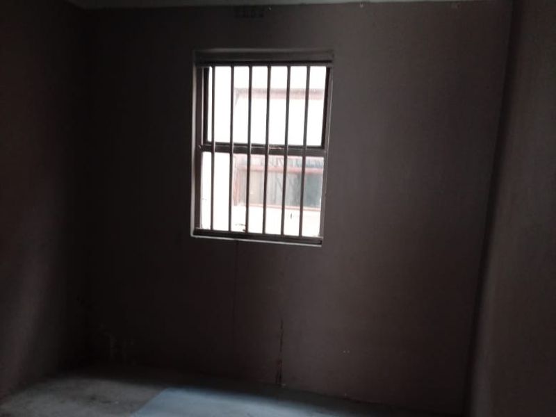 An empty bedroom featuring security bars on the window, requiring cosmetic updates and flooring repairs to improve the overall condition.