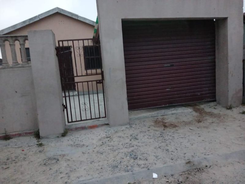 Front exterior view of the property featuring a roller garage door, metal pedestrian gate, and concrete boundary wall.