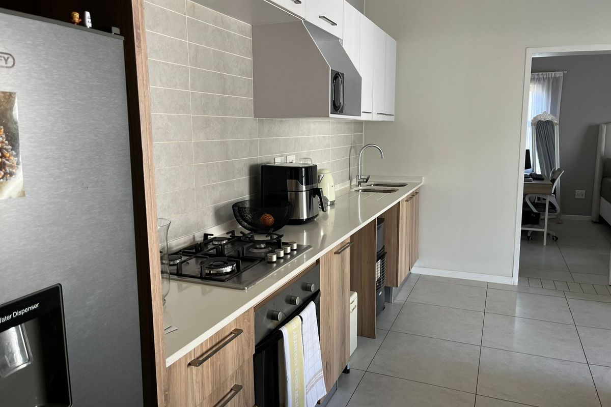 Modern kitchen featuring a gas hob, built-in oven, extractor fan, stone countertops, and sleek cabinetry with a tiled backsplash.