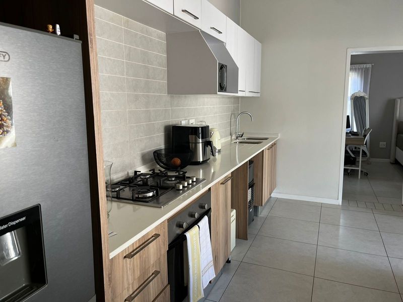 Modern kitchen featuring a gas hob, built-in oven, extractor fan, stone countertops, and sleek cabinetry with a tiled backsplash.