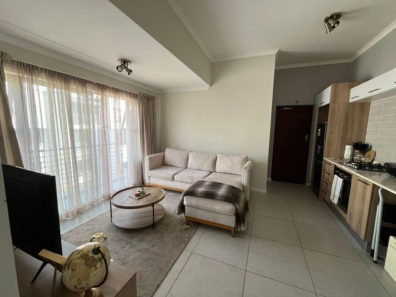 Modern open-plan living area featuring tiled floors, a contemporary kitchen with built-in appliances, and direct access to a balcony through sliding doors.