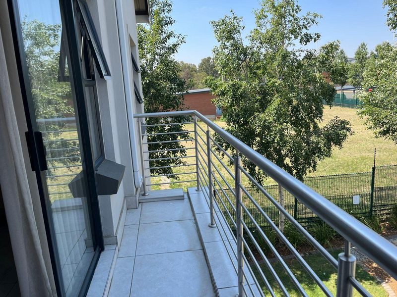 A clean, modern balcony featuring tiled flooring and a stainless steel balustrade, offering an open view of the surrounding greenery.