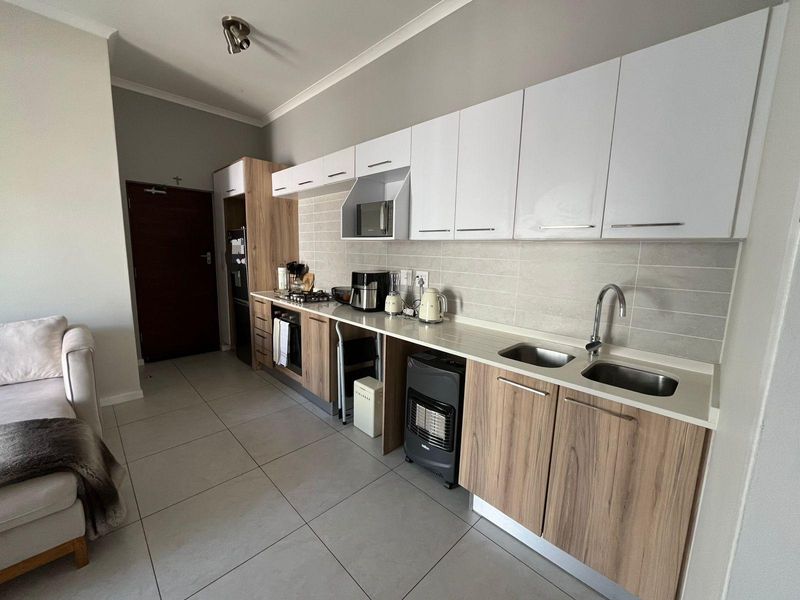 Modern open-plan kitchen featuring wood-grain and white cabinetry, stone-look countertops, double sink, and integrated gas hob, seamlessly connected to the living area.