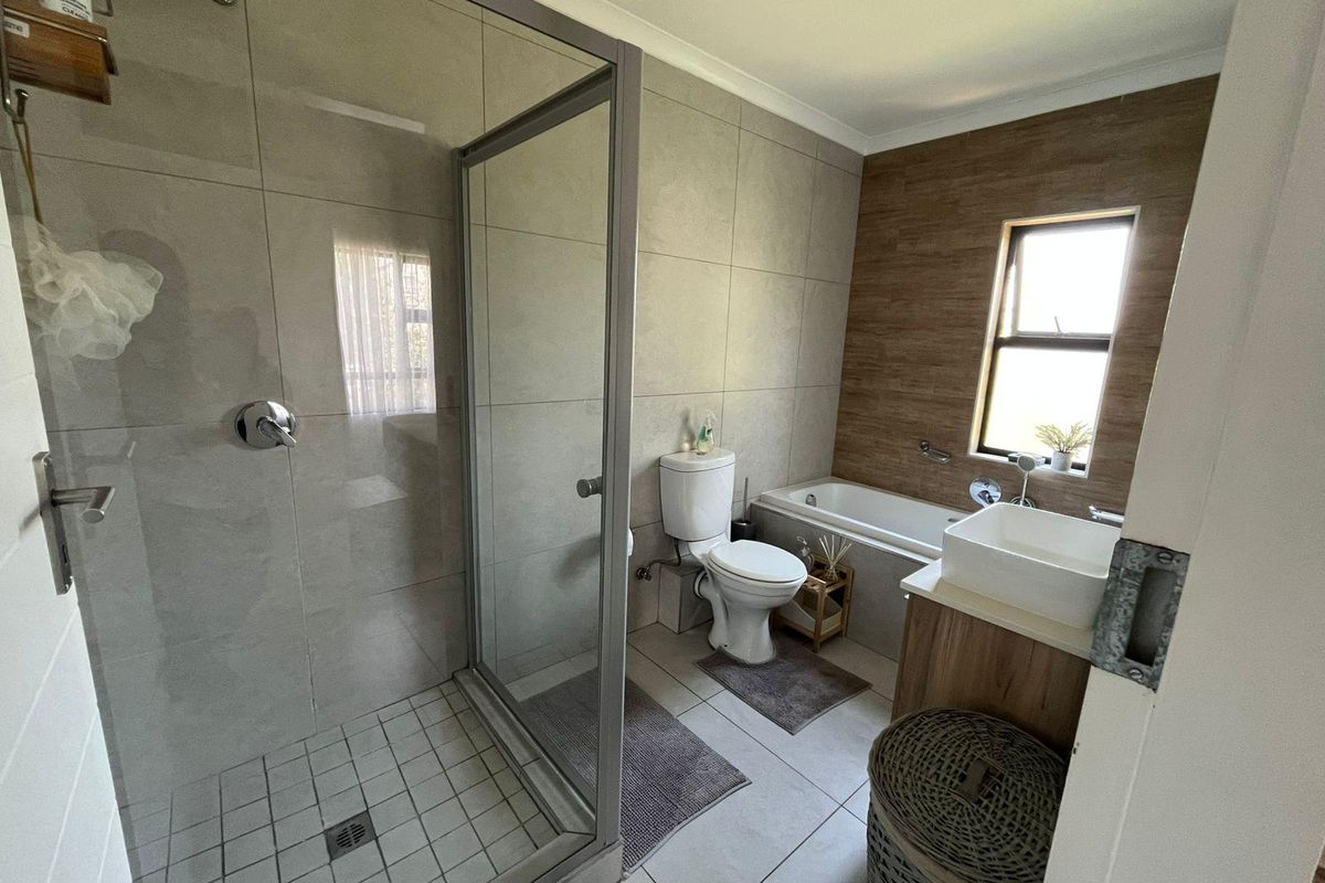 Modern bathroom featuring a glass-enclosed shower, a separate bathtub, a vanity basin, and neutral wall and floor tiling.