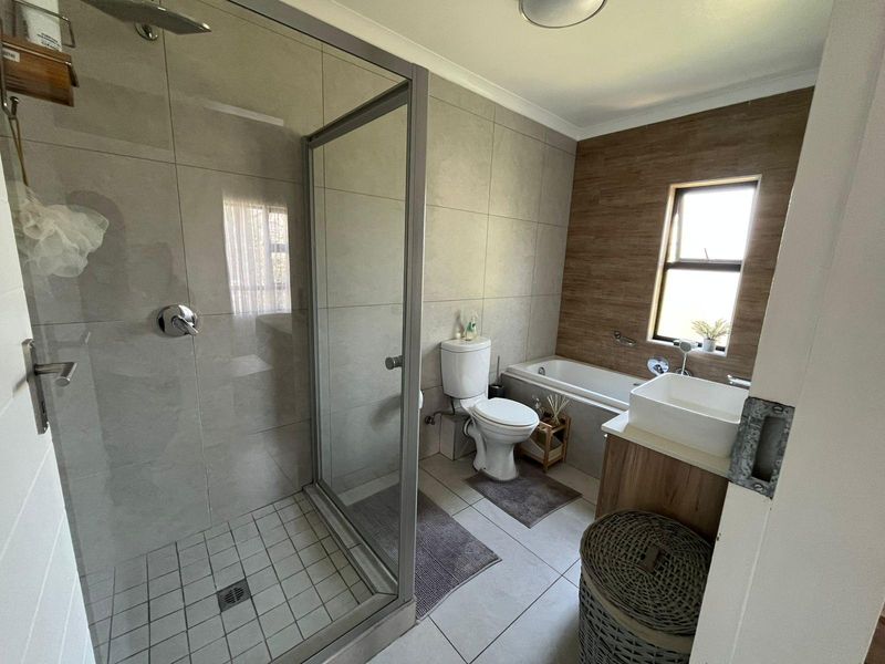 Modern bathroom featuring a glass-enclosed shower, a separate bathtub, a vanity basin, and neutral wall and floor tiling.