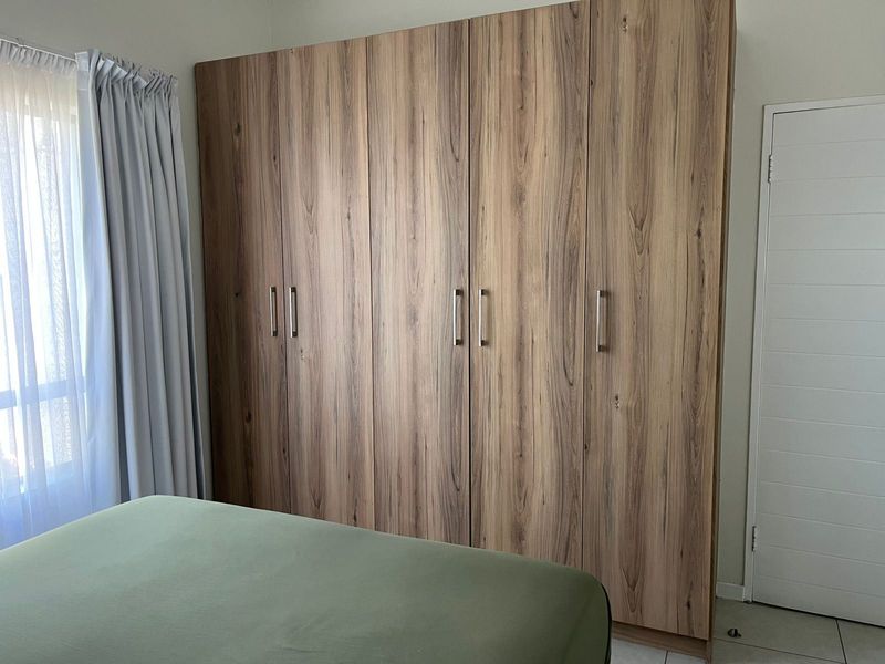 A bedroom featuring modern wood-grain built-in cupboards, tiled flooring, and neutral wall finishes.
