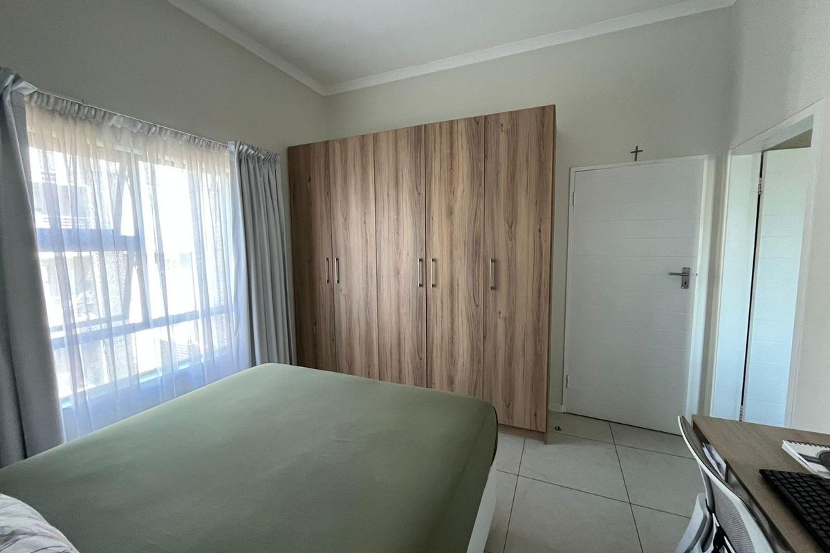 A well-maintained bedroom featuring neutral tiled flooring, large built-in wooden cupboards, and a window allowing for natural light.