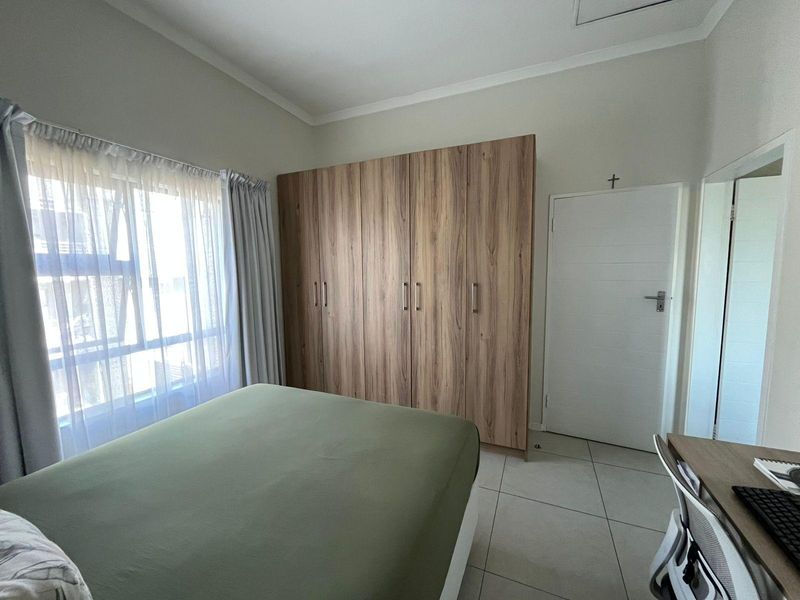 A well-maintained bedroom featuring neutral tiled flooring, large built-in wooden cupboards, and a window allowing for natural light.