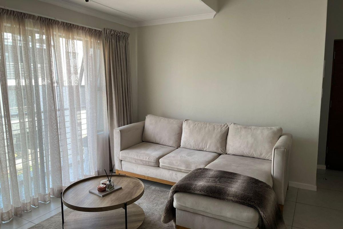 A bright living room featuring neutral tiled flooring, a recessed ceiling detail, and a large sliding glass door providing natural light.
