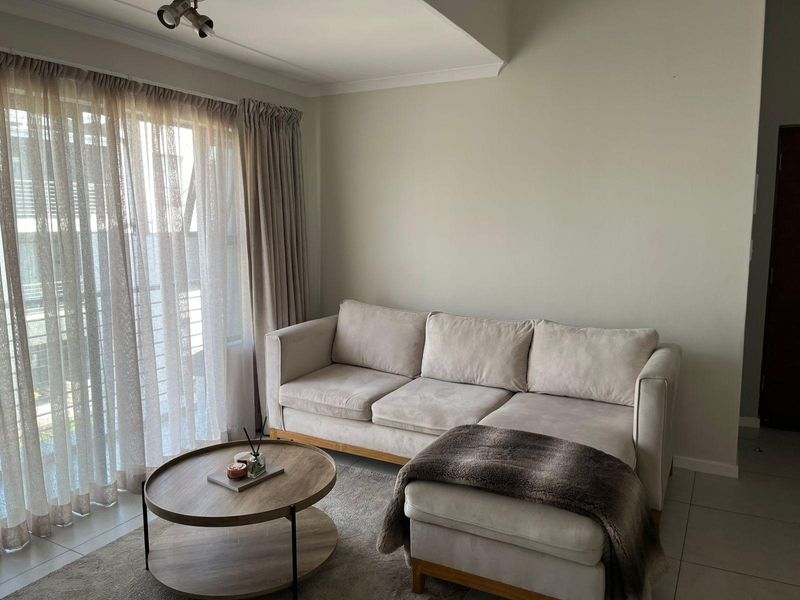A bright living room featuring neutral tiled flooring, a recessed ceiling detail, and a large sliding glass door providing natural light.