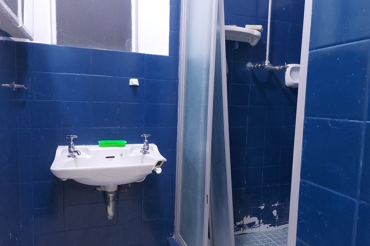 A dated bathroom featuring blue wall tiles, a wall-mounted basin, and a shower enclosure, currently in need of renovation and repairs.