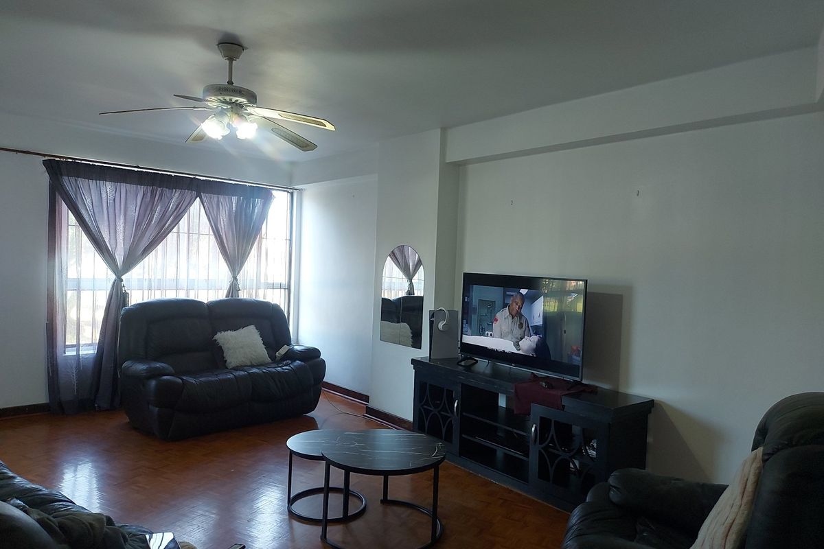 A spacious living room featuring parquet flooring, a ceiling fan, and large windows with security bars, offering a comfortable and functional living space.