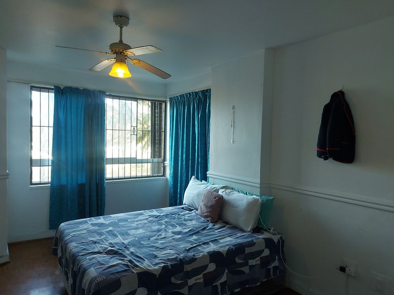 A bedroom featuring laminate flooring, a ceiling fan, and windows fitted with security bars.