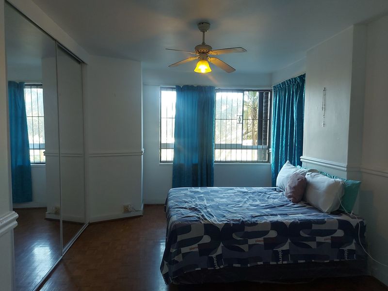 A bedroom featuring parquet flooring, a ceiling fan, and a large built-in mirrored wardrobe with security bars on the windows.