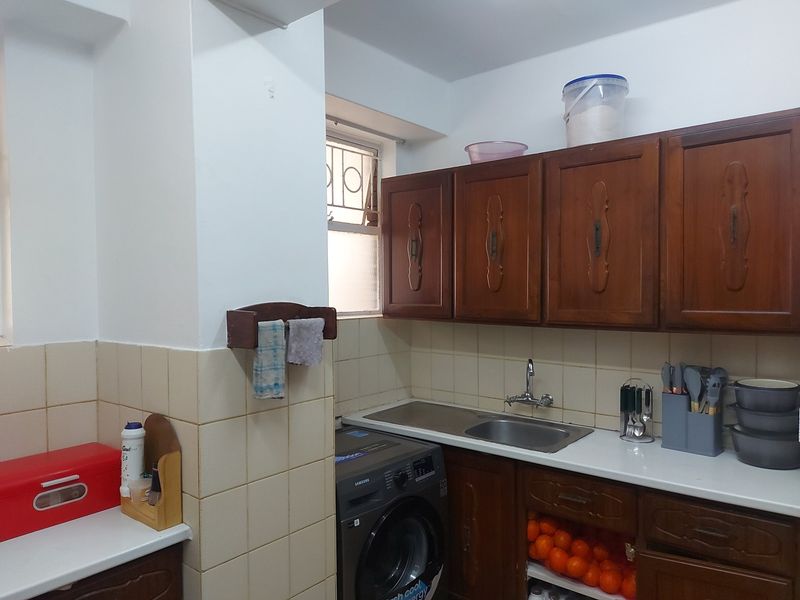 A functional kitchen featuring wooden cabinetry, a stainless steel sink, tiled backsplash, and a dedicated space for a washing machine.