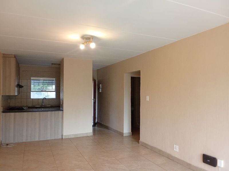 An open-plan living and kitchen area featuring tiled flooring, neutral walls, and a functional kitchen with built-in cabinetry and integrated appliances.