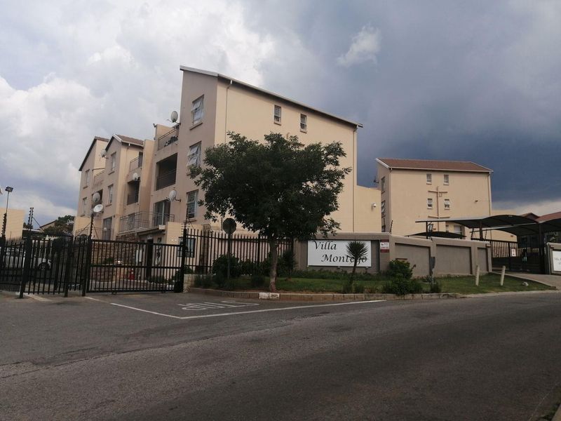 Street view of the Villa Montejo townhouse complex, featuring multi-story residential buildings, secure gated access, and paved driveway areas.