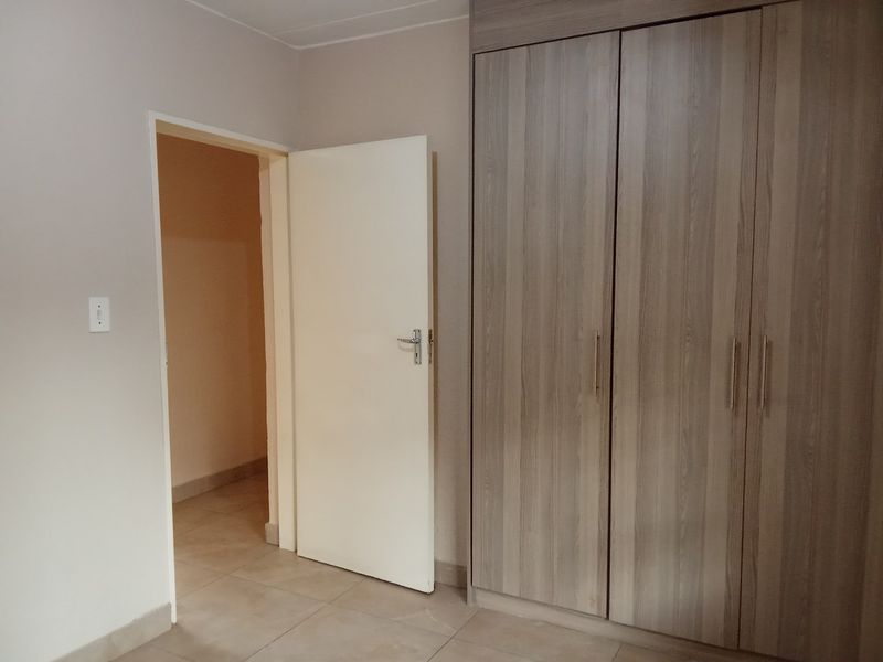 A clean, empty bedroom featuring modern wood-finish built-in cupboards and neutral tiled flooring, offering a versatile space ready for personalization.