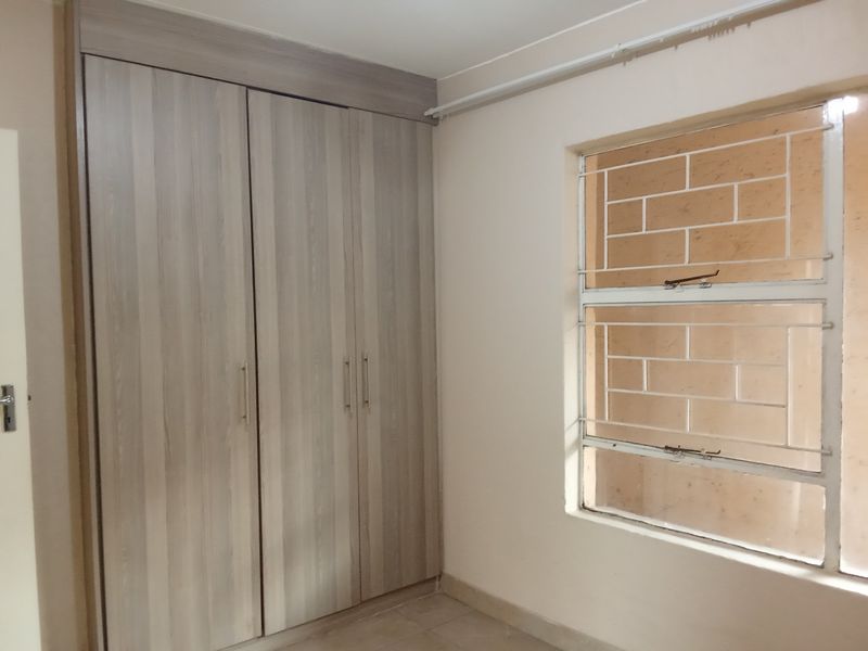A clean, empty bedroom featuring a modern wood-finish built-in wardrobe and a window fitted with security bars.